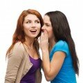 two smiling girls whispering gossip